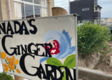 温室内の棚に並んだ鉢植えの前に手描きの看板にCANADA'S GINGER GARDEN と書かれたガーデンディスプレイ