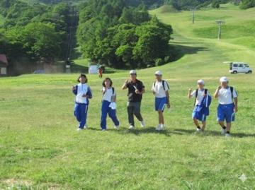 青い半ズボンと白い上着を着た六人が広い芝生の斜面を並んで歩いている風景