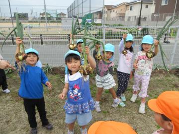 畑の前で収穫した根菜を手に持って並んでいる
