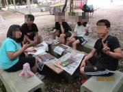 公園の木陰でベンチに座り新聞や資料を広げて焼き板の完成を喜ぶ様子