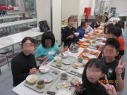 食堂の長いテーブルに並んで座り給食のトレーや丼を前にして食事をしている子どもたちのグループの写真