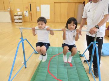 男の子と女の子が2人で鉄棒に顎を掛けて、腕の力でぶら下がっている様子