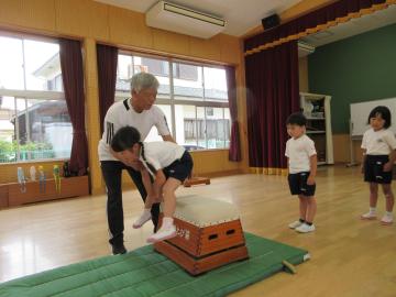 女の子が、体操の先生に支えられながら跳び箱を跳んでいる様子