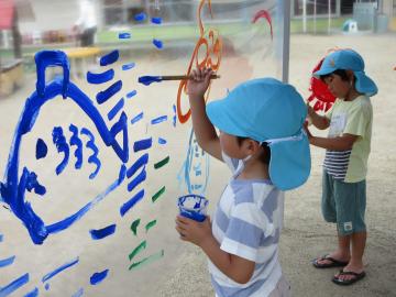 男の子が、青い絵の具で魚と水の流れを描いている様子