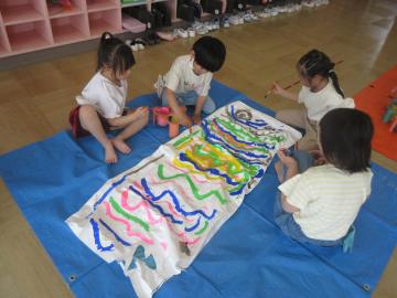 友達と一緒に大きなこいのぼりに絵の具で絵を描く子供たちの様子