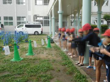 赤い帽子をかぶった列の人々が校舎の軒下に並んで的に水を当てている