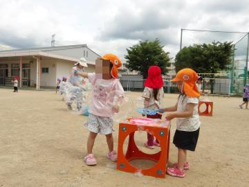 屋外で、3歳児の子どもたちがカラフルな遊具の上に置いたシャボン玉液で、シャボン玉を作って遊んでいる様子