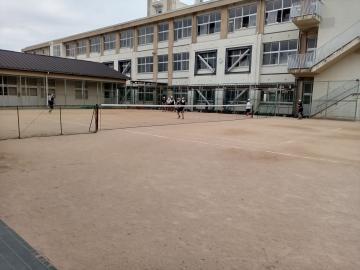 校舎を背景に運動場で数人の児童が遊んでいる学校の屋外風景