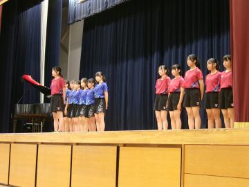 体育館の壇上で、女子卓球部の生徒たちが決意表明をしている様子