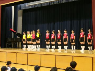 体育館の壇上で、女子バレーボール部の生徒たちが決意表明をしている様子