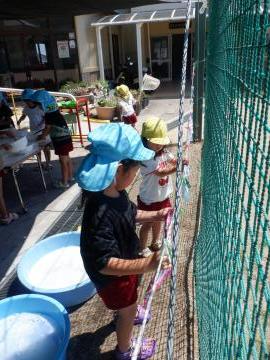 洗濯ごっこで洗った布をロープに掛けて干して洗濯ばさみでとめる子供たち
