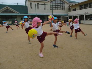 サッカーボールを持った手を伸ばし、片足をあげて体をとめる子供たち
