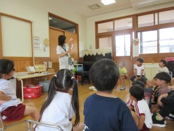 歯の模型を使って歯磨きの仕方を伝える園長と、椅子に座って話を聞く子供たち