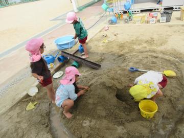 砂場に穴を掘って川を作ったり、砂山にトンネルを作ってのぞいたりしている子供たち