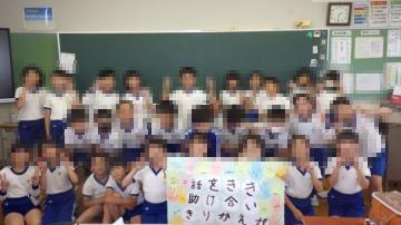 4年生が教室の黒板前で集合写真を撮っている様子