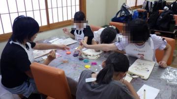 室内で、トートバッグに絵付けをしている児童たちの様子