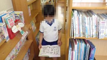室内で、本棚と本棚のすきまで、本を集中してよんでいる児童の様子