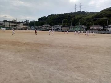 広い土の運動場でユニフォームを着た選手たちがサッカーの練習をしている風景
