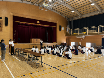 体育館内で、生徒会長が参加者に生徒会規約の改正点を説明している様子です。