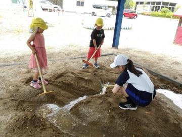 幼児と中学生が砂場で水路づくりをする様子