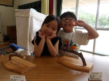 幼児が木彫りの野鳥と一緒に写真を撮る様子