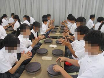 生徒たちが教机に向かい合って座りロクロ台のような台で粘土を手で成形している