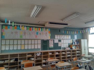 小学校の教室で窓際に掲示物や短冊が飾られ黒板と棚と机が整然と並ぶ様子