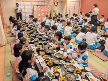 旅館の和室に並べたテーブルに生徒が整列して座り豪華な夕食を食べている様子