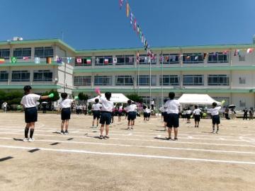 国旗が掲げられた校庭で操服を着た多数の児童がダンスの練習をしている様子