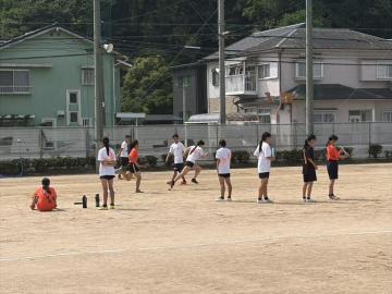 住宅街を背にした運動場でユニフォーム姿の生徒たちがボールを使って練習している様子