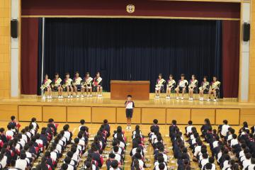 体育館の前に立つ生徒と舞台上に座る候補者とそれを座って見ている全校生徒