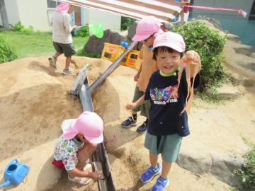 園庭の築山でタフロープをそうめんに見立て、そうめん流しをしている園児たちの様子