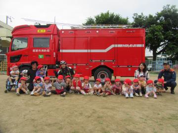 園庭で、3歳児たちが消防車の前で集合写真を撮っている様子