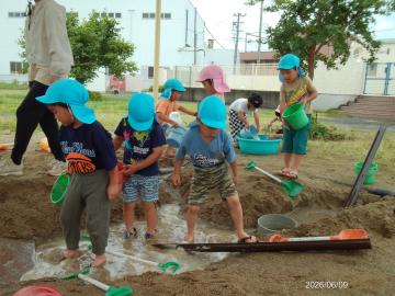 幼児が砂場で水を流して遊んでいる様子