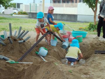 幼児が砂場で樋を使って水を流そうとしている様子