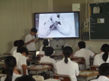 画面に自分の作品を映して発表する生徒と、机に座って発表を聞いている生徒たちの様子