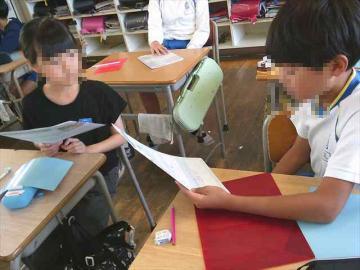 教室の机に座り二人の子どもが書類を手に会話している様子
