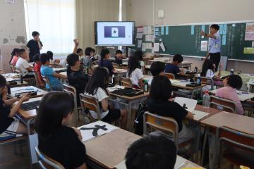 教室内で、講師がこれから書く大の字について児童たちに説明している様子