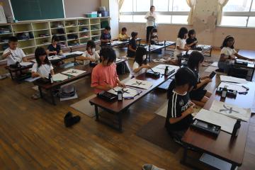 隣の部屋で児童たちが正座で字を書いている様子