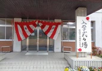 校舎の入口に赤と白の横断幕が飾られ入口横に入学式会場と書かれた縦長の看板が立っている