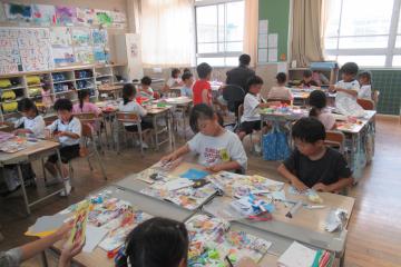 1年生が図画工作の授業で折り紙を折って切り落とし広げて作品を作っている様子
