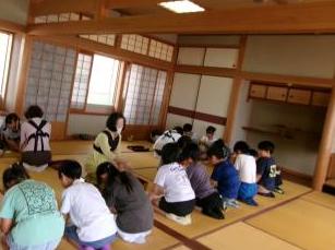 和室の畳の上に座って茶道教室をする児童たちと指導者が並んでいる様子