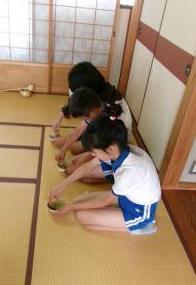 和室で、体操服を着た児童たちが並んで座りそれぞれお茶をたてている様子