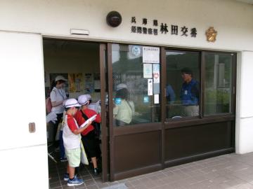 白い帽子をかぶった児童たちが交番の窓口越しに警察官と話している様子
