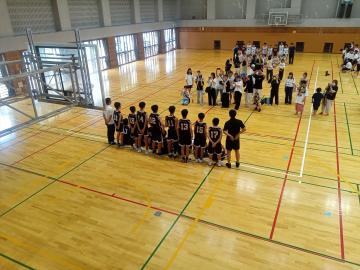 屋内の体育館で複数の子どもたちが制服や運動着でグループごとに列を作って整列している様子