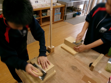 生徒がテーブルの上で木材を使って作業している様子