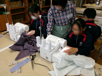 白い布をテーブルに広げてミシンを使って作業する生徒と講師