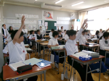 教室で席に座った生徒達が挙手をしている授業風景