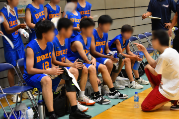 体育館内で、男子バスケットボール部の選手がタイムアウトの時、監督より指示を受けている様子です。