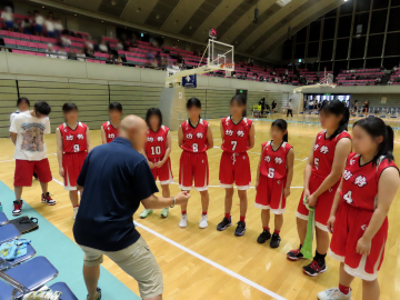 体育館内で、女子バスケットボール部の選手がタイムアウトの時、監督より指示を受けている様子です。